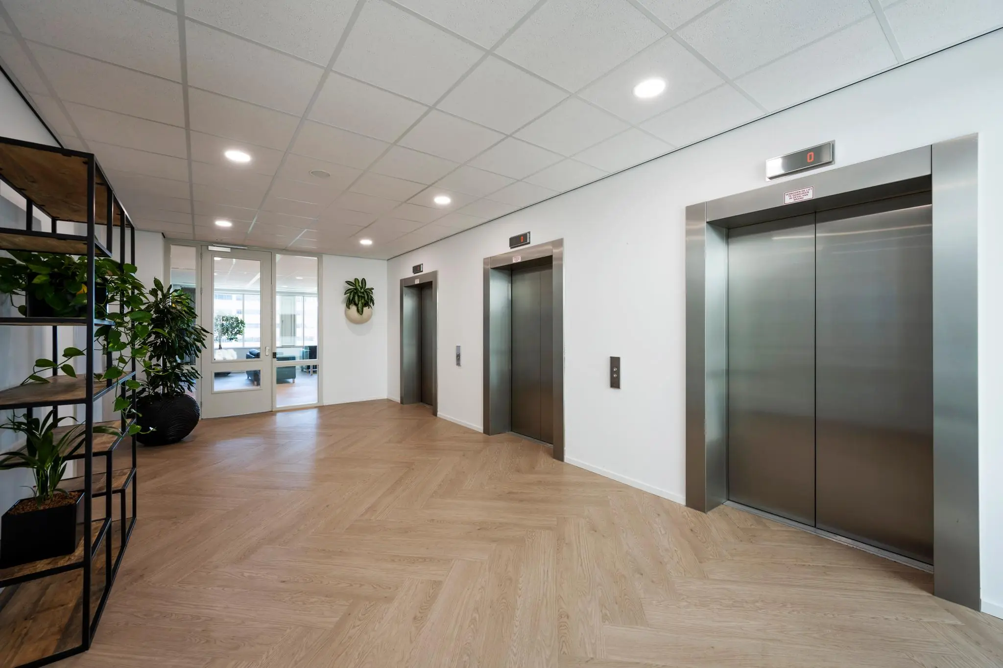 Moderne liftlobby met drie rvs-liften en houten visgraatvloer in een kantoorgebouw aan de Thomas R. Malthusstraat.